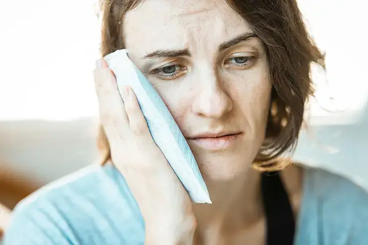 Mujer con expresión de molestia y la mano en la mejilla, mostrando dolor de muela.