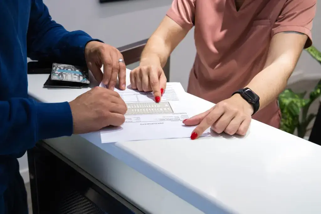 Persona revisando junto a una profesional de clínica dental un presupuesto y plan de tratamiento odontológico sobre un mostrador.
