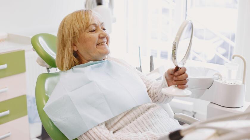 Mujer sentada en el sillón dental mirándose en un espejo