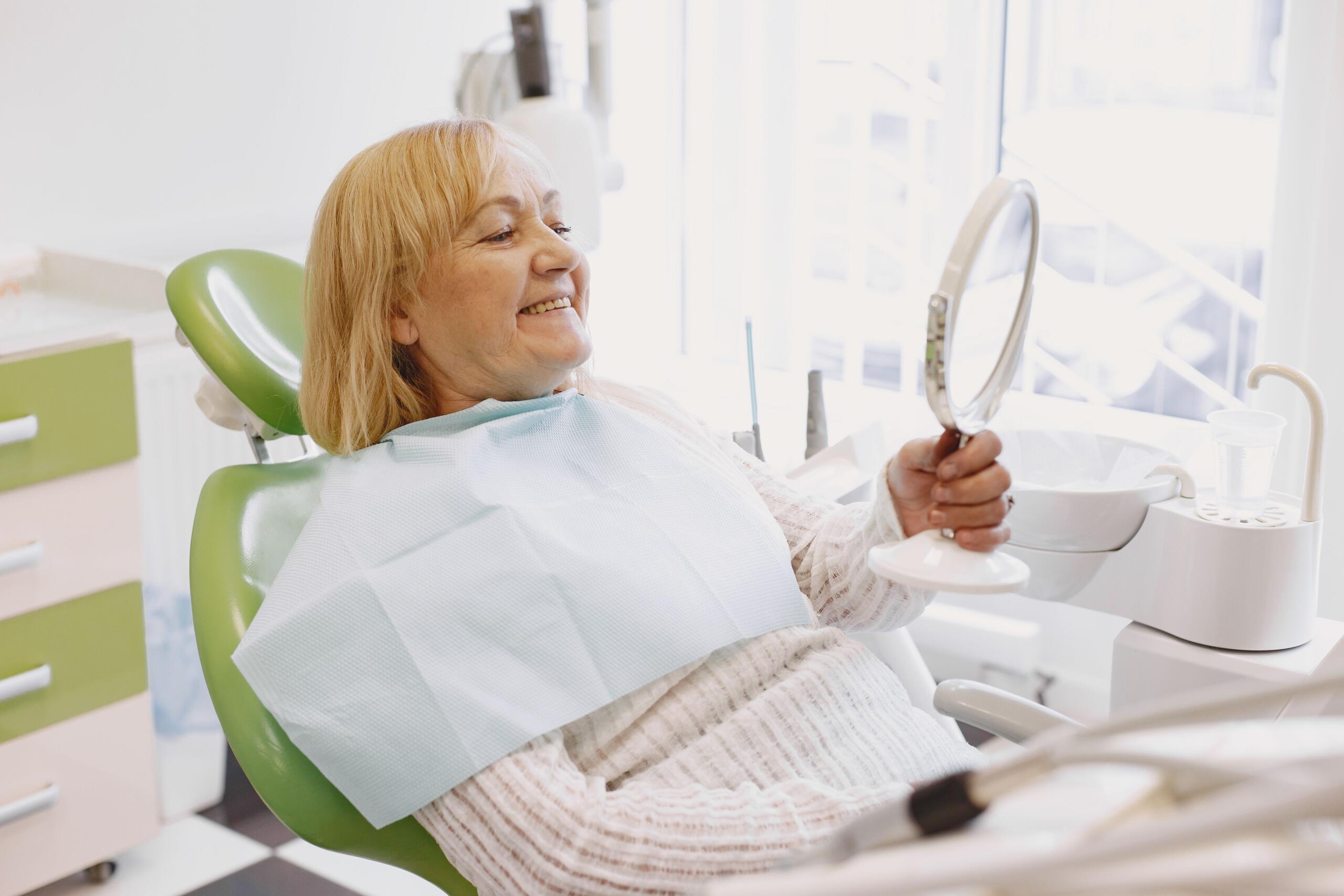 Mujer sentada en el sillón dental mirándose en un espejo